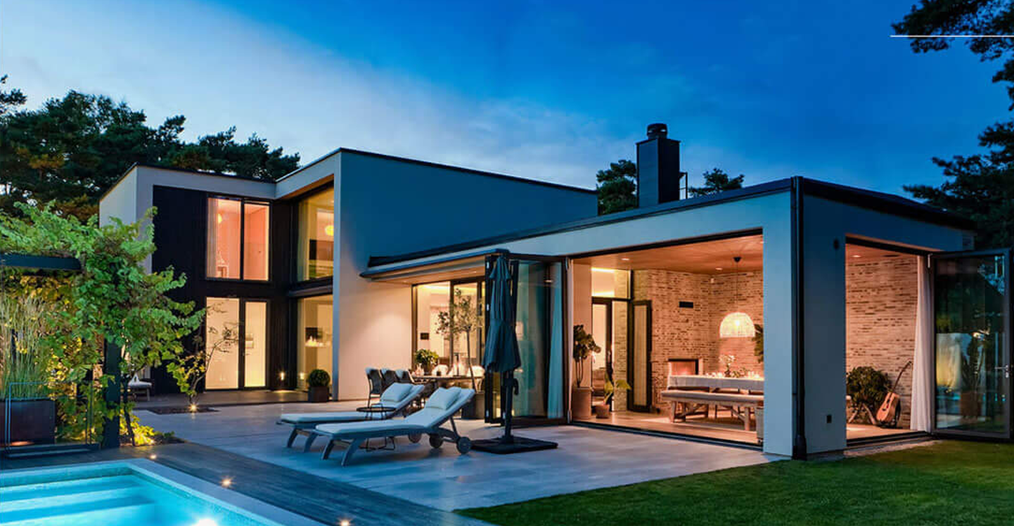 Modern luxury villa at dusk with large glass sections, pool and patio